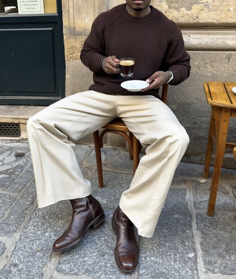Brown ribbed jumper, cream wide trousers and brown boots at a café table with an espresso