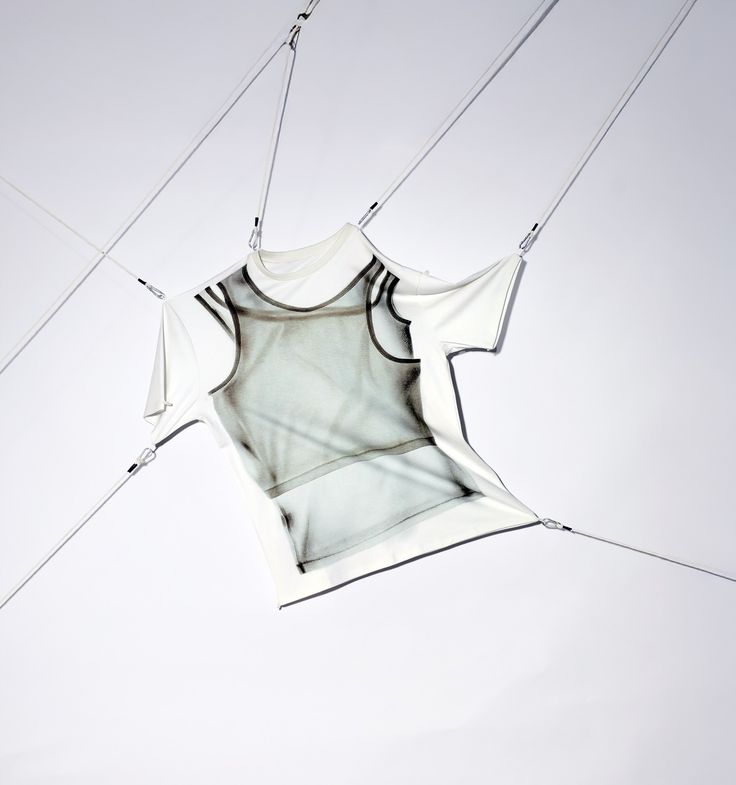 A white T-shirt suspended in mid-air by thin cords against a pale backdrop